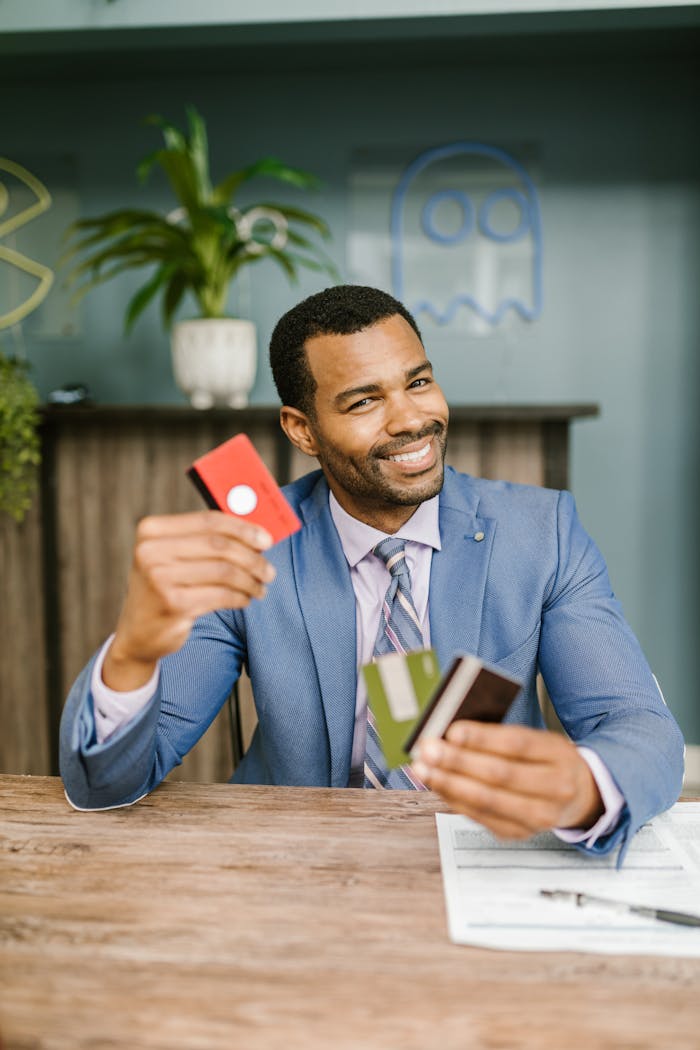 creative Smiling man in suit holding credit cards at a desk indoors, showcasing financial confidence.