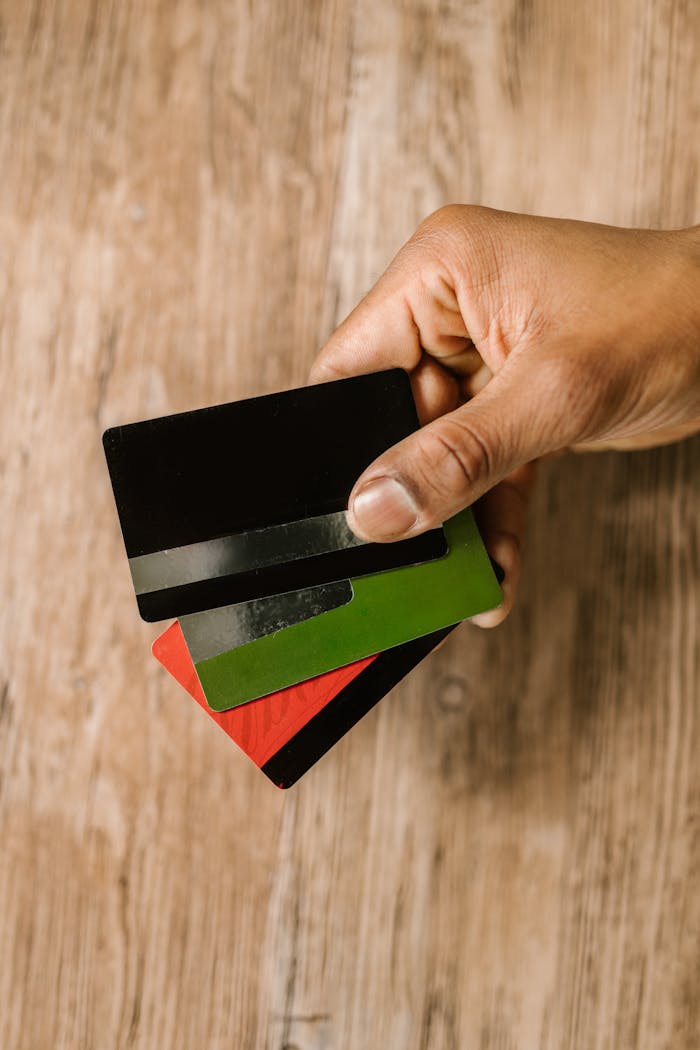 Services-02 A hand holding multiple credit cards on a wooden background, emphasizing payment and finance themes.