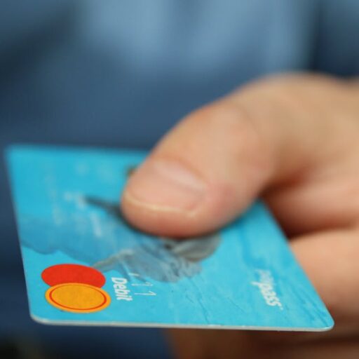 A close-up shot of a hand offering a blue debit card for payment.