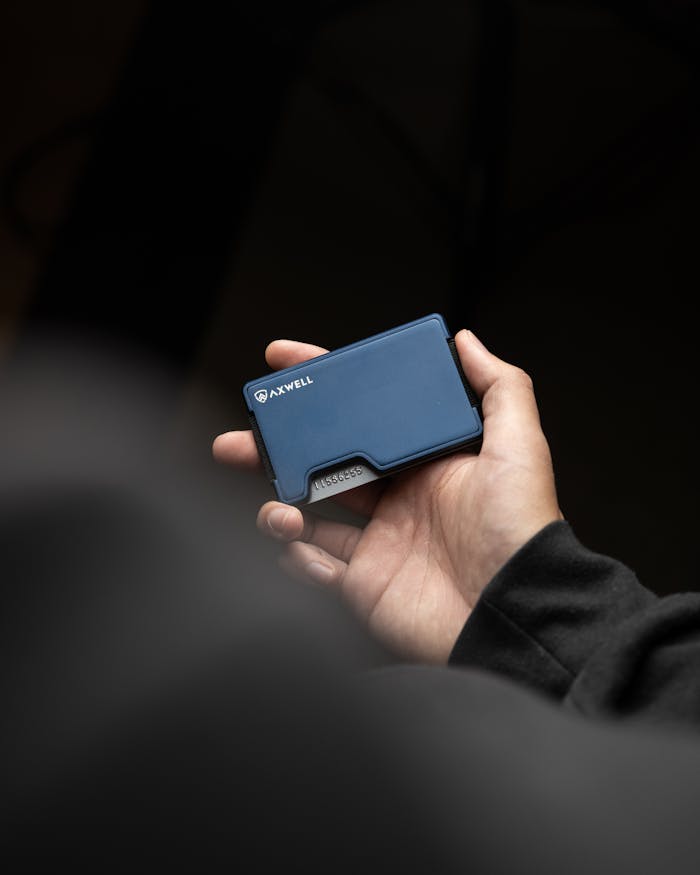 digital A persons hand holding a sleek, blue wallet against a dark background.