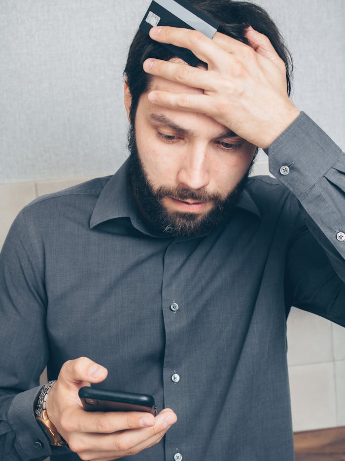 our-story A stressed man looks at his smartphone, holding a credit card in his hand.