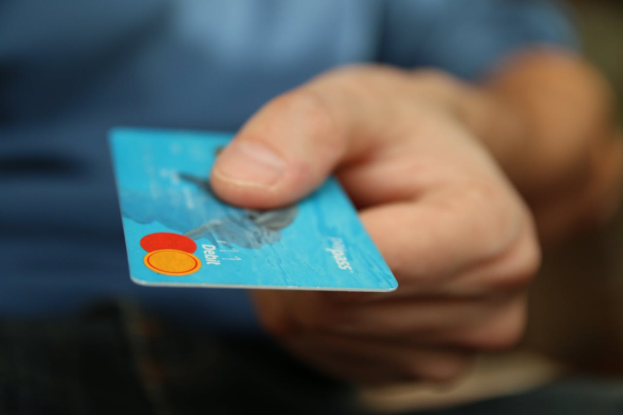 creative-02 A close-up shot of a hand offering a blue debit card for payment.